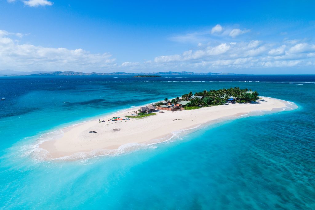 Aerial view of Fiji coastline with surfers riding waves – Atoll Travel