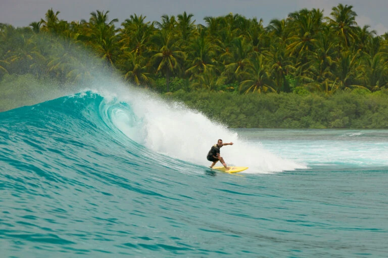 Surfer riding wave during Hakuraa surf trip, Maldives tropical backdrop – Atoll Travel
