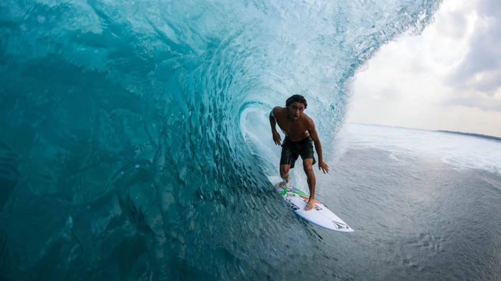 Surfer performing aerial maneuver over clear wave, Maldives – Atoll Travel